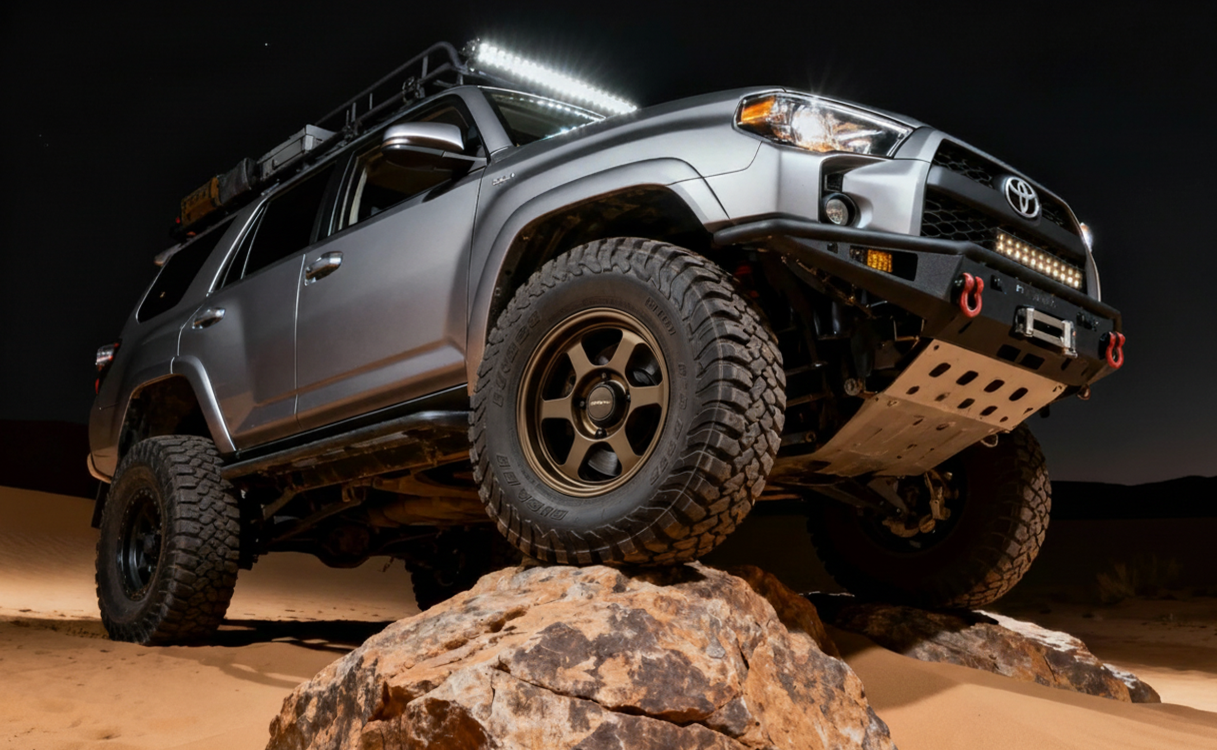 Lifted Toyota 4Runner climbing a rock at night, low angle with roof light bar
