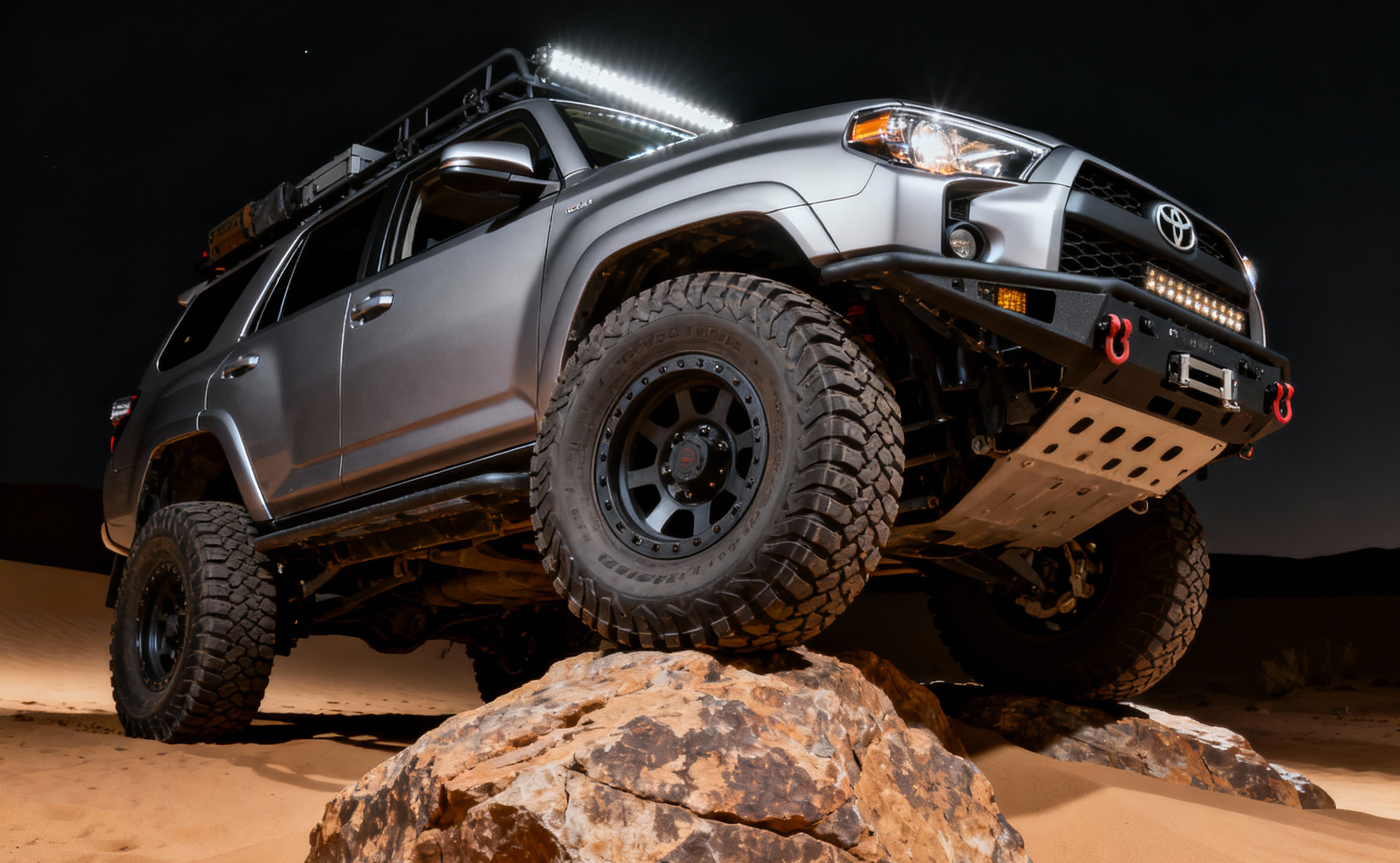 Lifted Toyota 4Runner climbing a rock at night, low angle with roof light bar